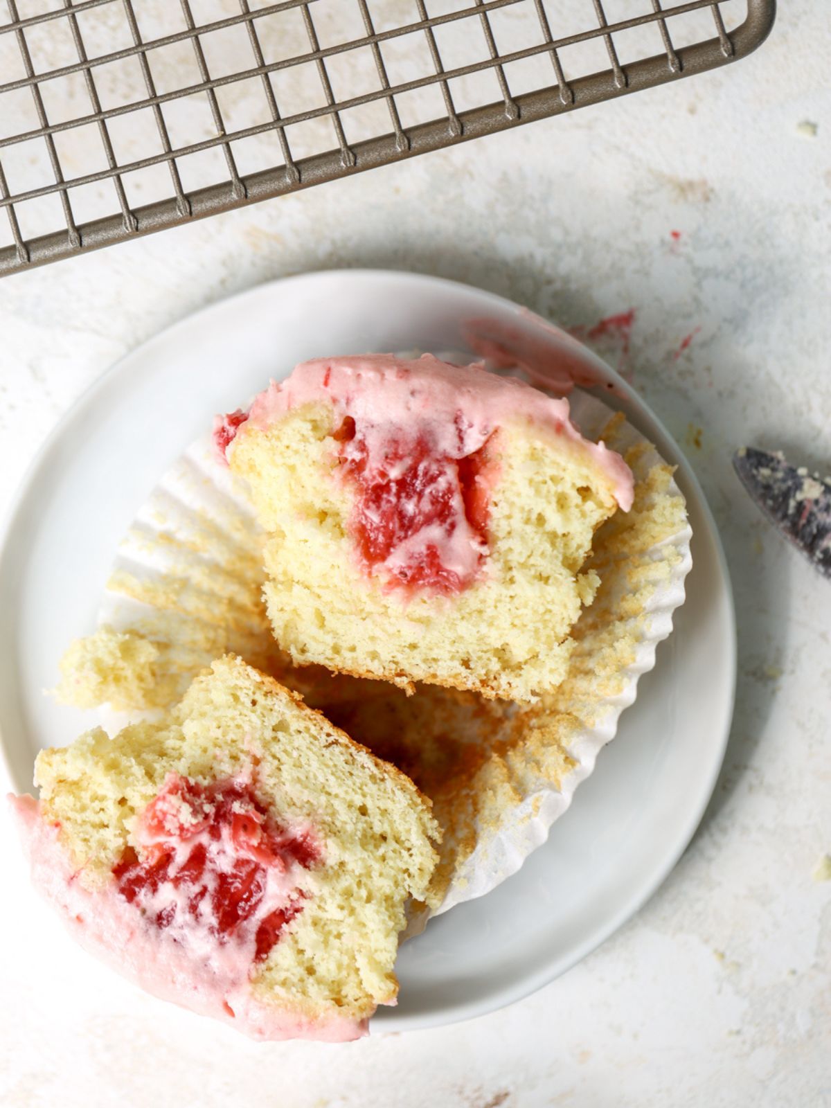A frosted strawberry cupcake cut in half on a plate.