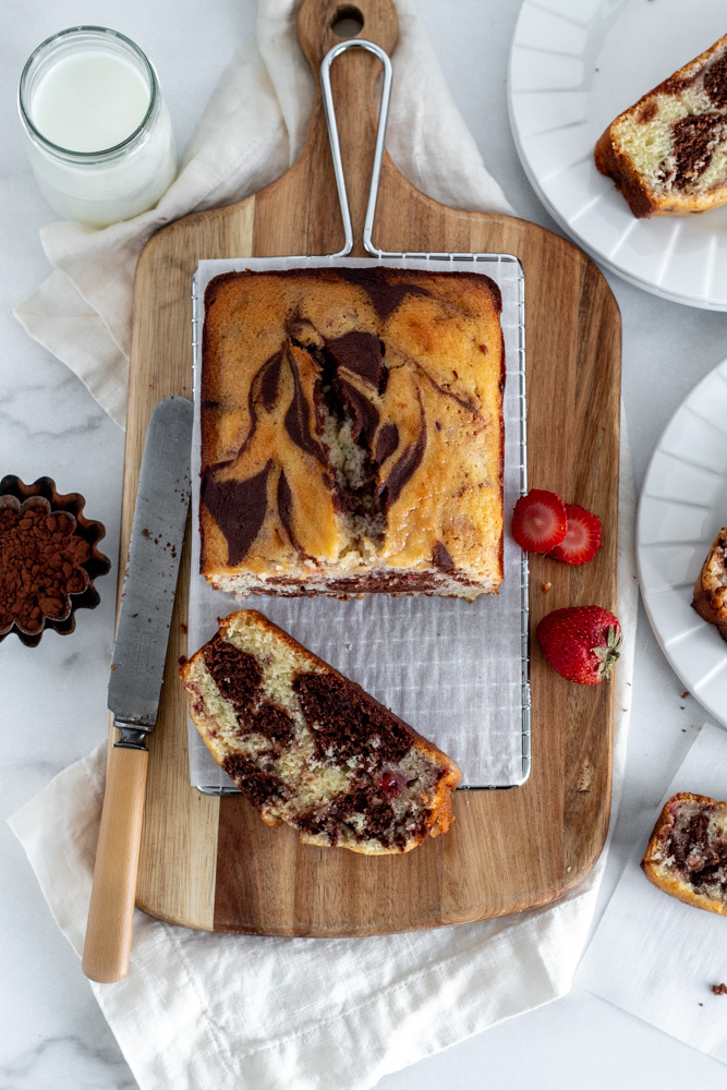 A Neapolitan marble cake on a rack with a slice, a knife and some strawberries beside it.