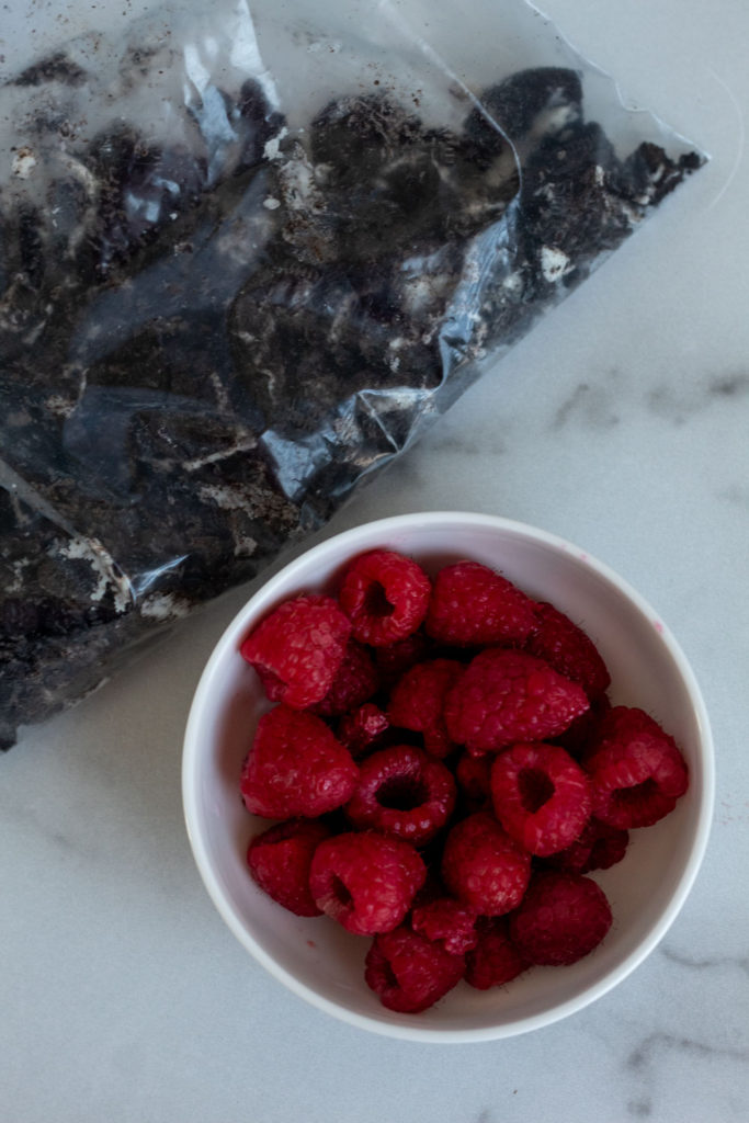 A white bowl filled with fresh raspberries and a bag of crushed Oreo cookies. 