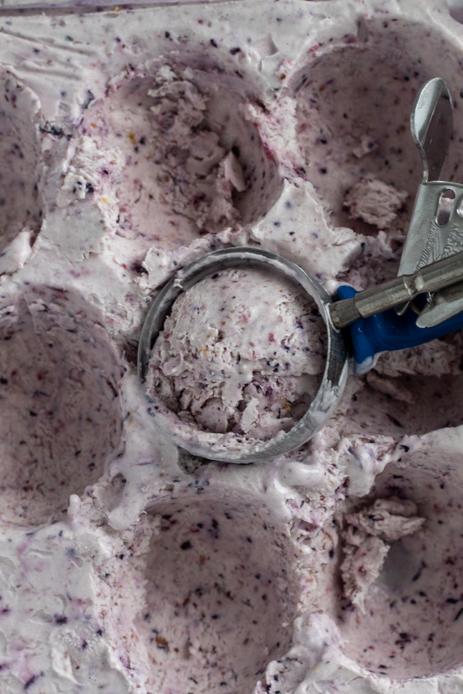 An ice cream scoop in a pan of purple colored berry ice cream.