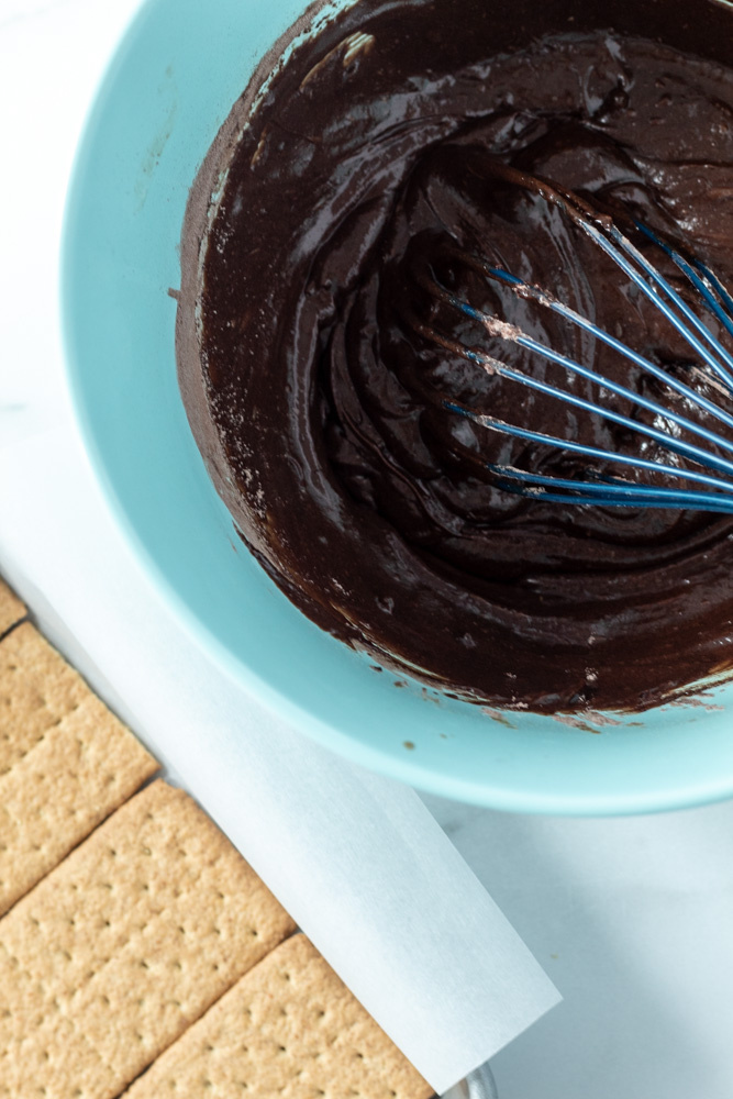 Brownie batter being mixed with a whisk in a bowl with some graham crackers nearby.