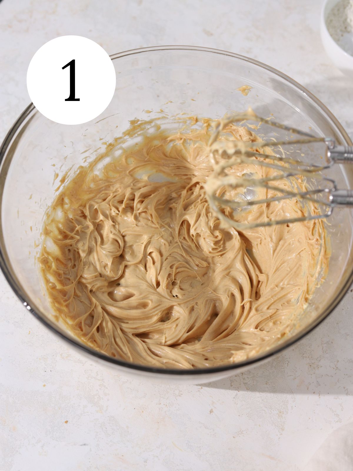 Peanut butter and butter mixed together in a bowl with an electric mixer.