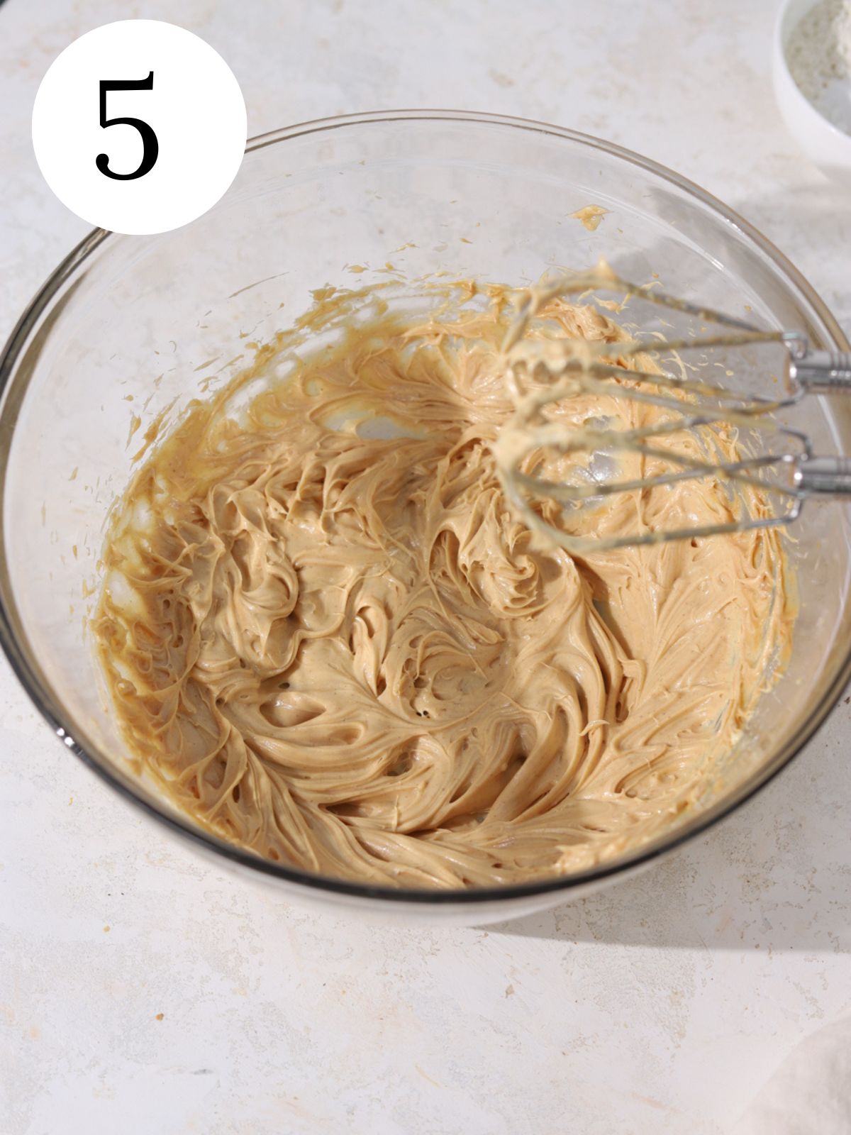 A large glass bowl with peanut butter frosting and an electric mixer.