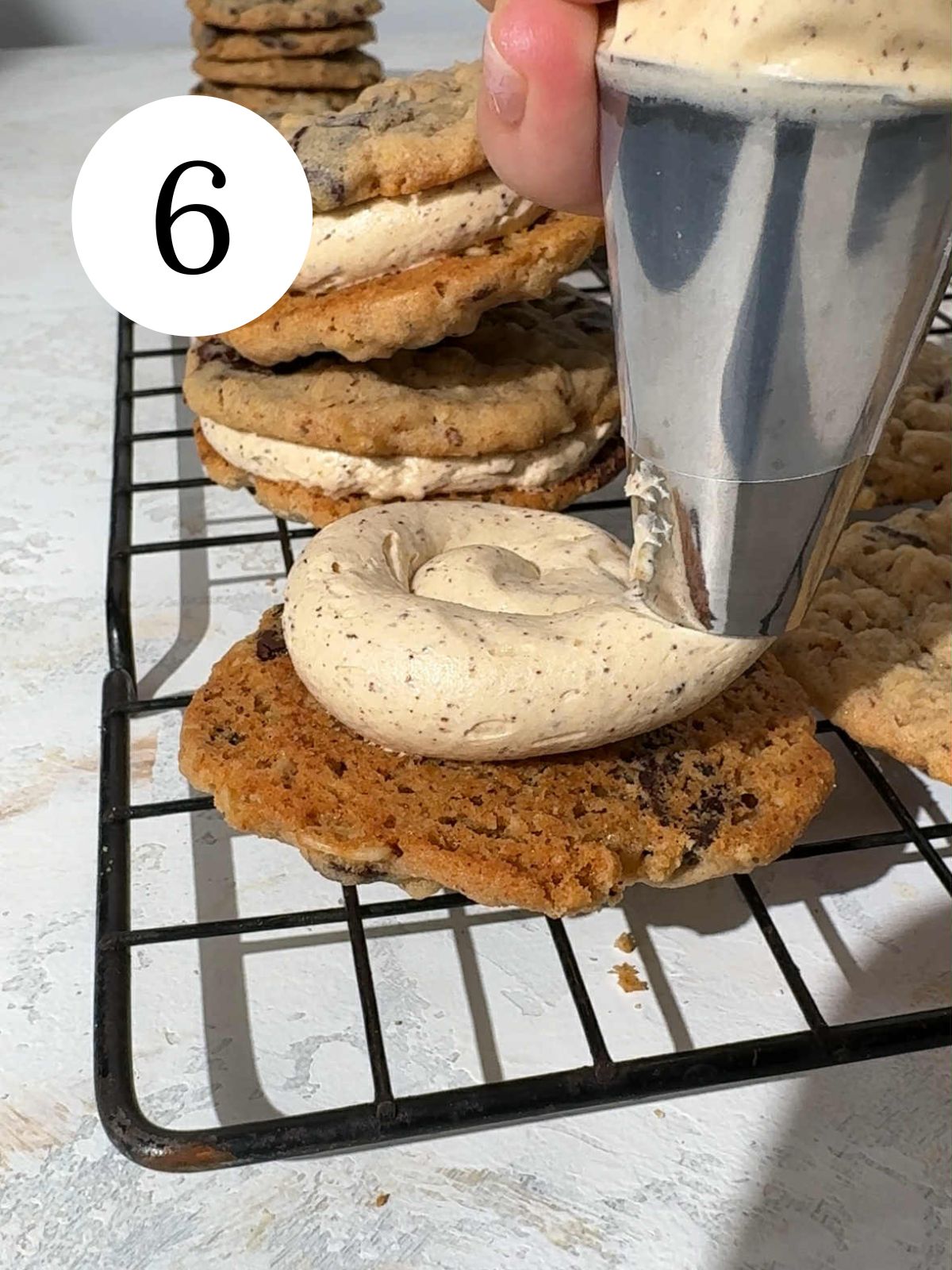 Oatmeal cookies on a rack with frosting being piped on top.