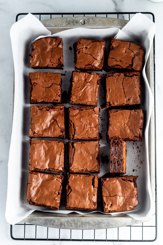 Chocolatey brownies cut into squares  in a rectangular pan lined with parchment paper.