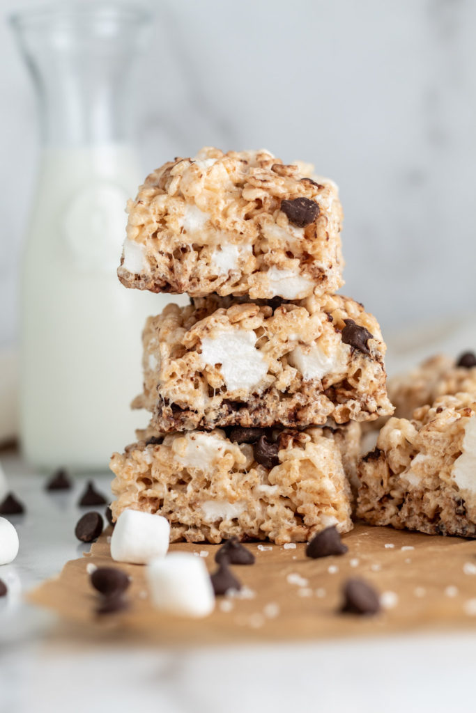 A stack of three chocolate chip rice krispie treats in front of a jug of milk. 