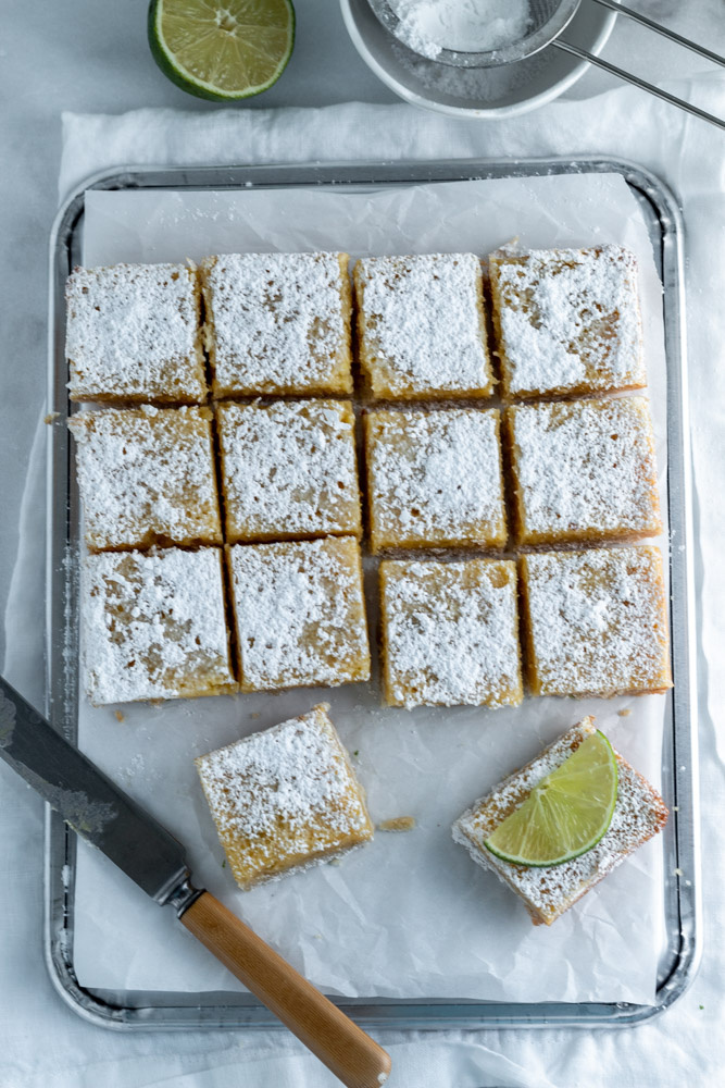 Tangy sweet lime bars topped with powdered sugar with a knife nearby. 