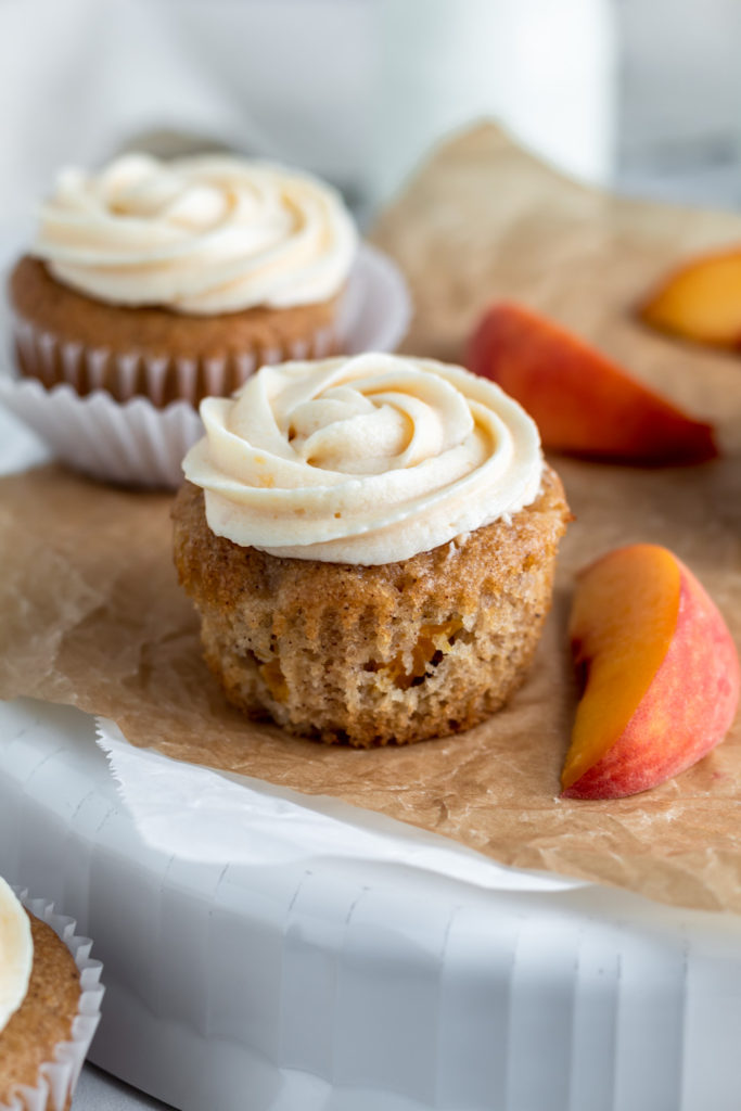 A cupcake with pieces of peaches baked in it and frosting on top. 