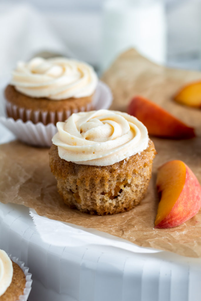 A frosted peach cupcake next to a peach slice 