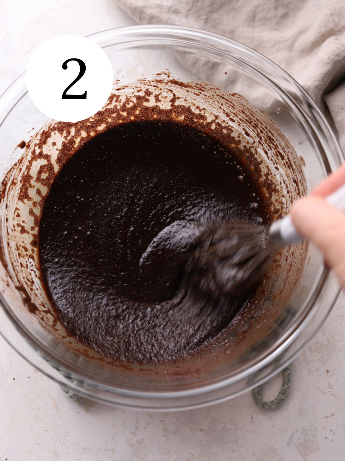 A glass bowl with cocoa powder and melted butter being whisked together. 