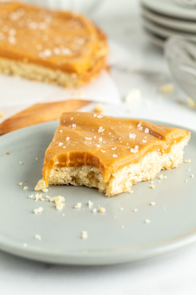 a slice of shortbread topped with ganache and topped with sea salt with a bite in it. 