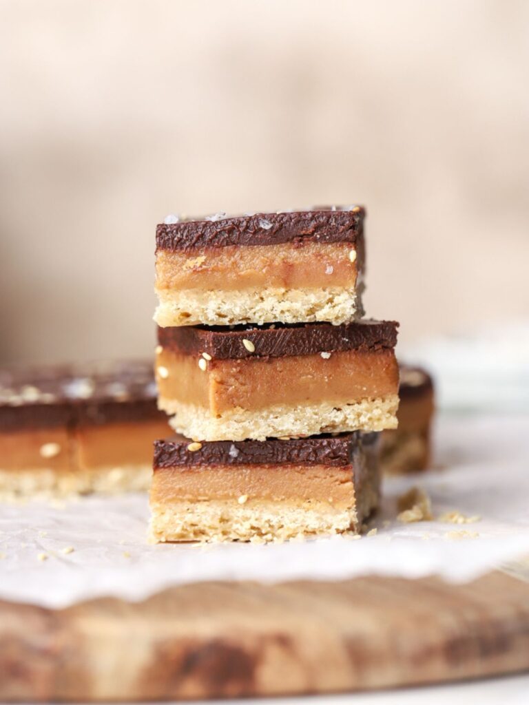 A stack of three millionaire bars topped with sea salt on parchment paper. 