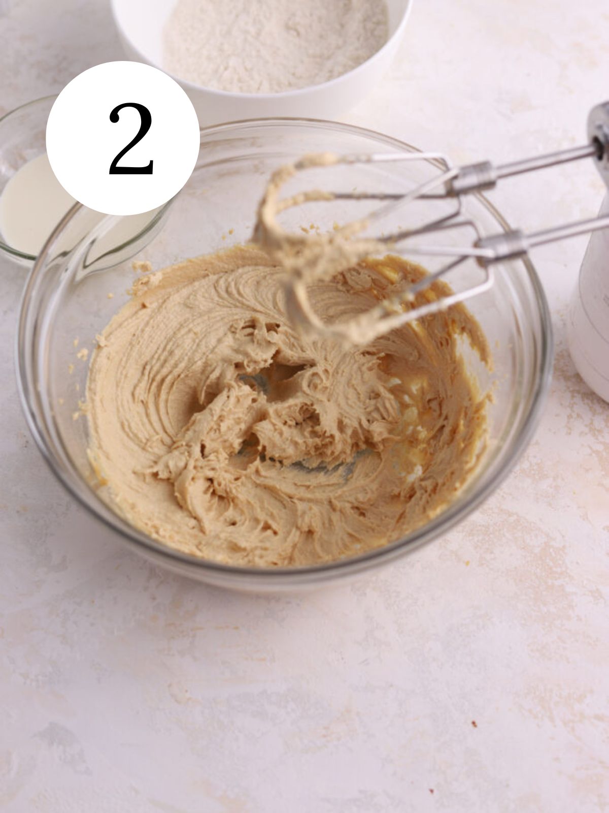 A glass bowl with peanut butter and butter mixed together with an electric mixer.