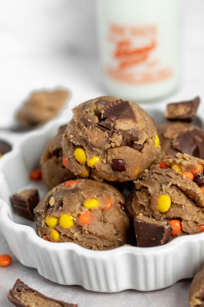 A close up of cookie dough with reese's pieces and chopped peanut butter cups in a bowl.