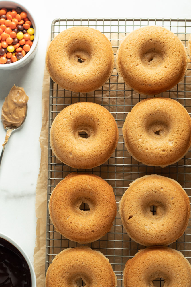 peanut butter donuts on a rack with a spoonful of peanut butter and reese's pieces nearby.
