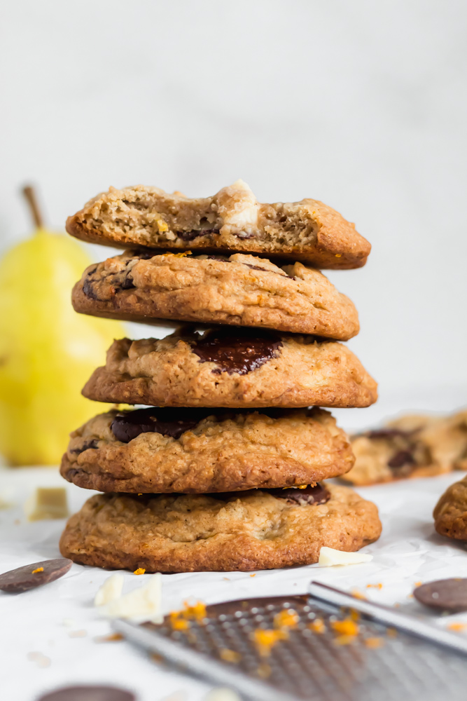 A stack of cookies baked with pears and chocolate with a pear behind it. 