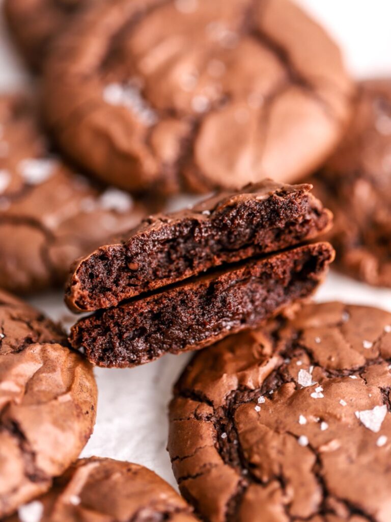 A chocolate cookie split in half and a batch of chocolate cookies.