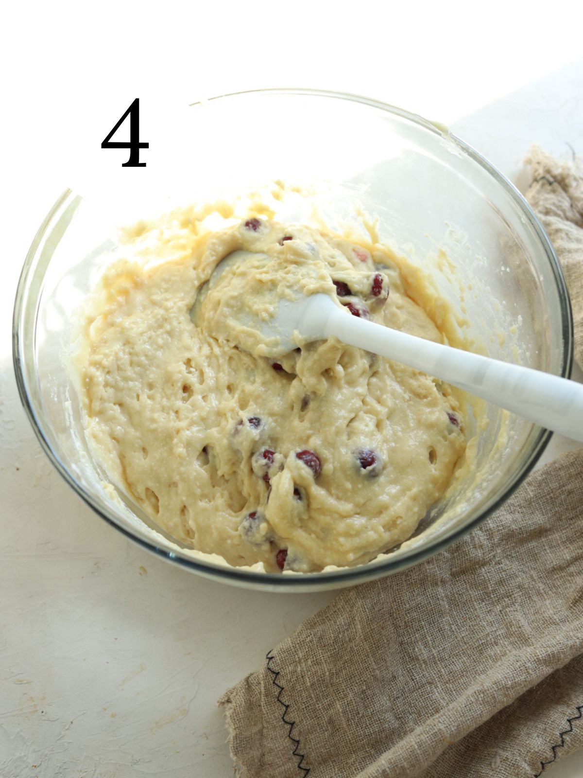 A glass mixing bowl with cranberry cake batter and a spatula.