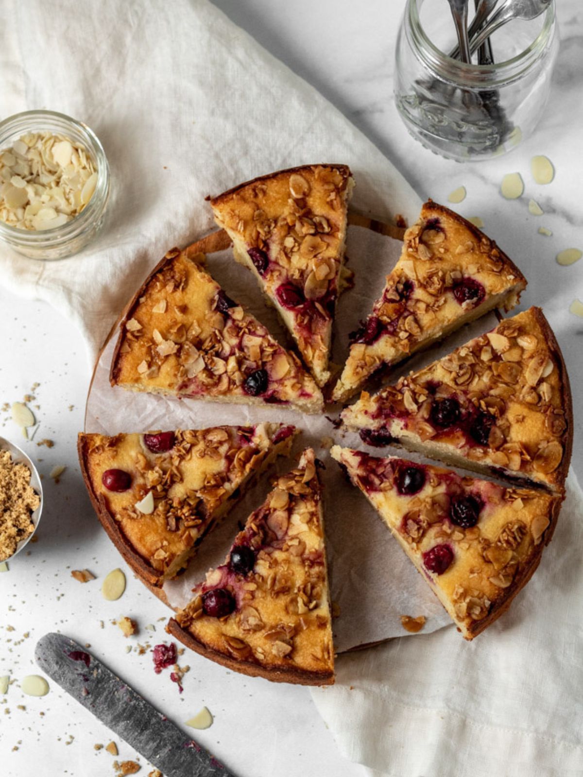 A round cake topped with cranberries and almonds cut into slices.