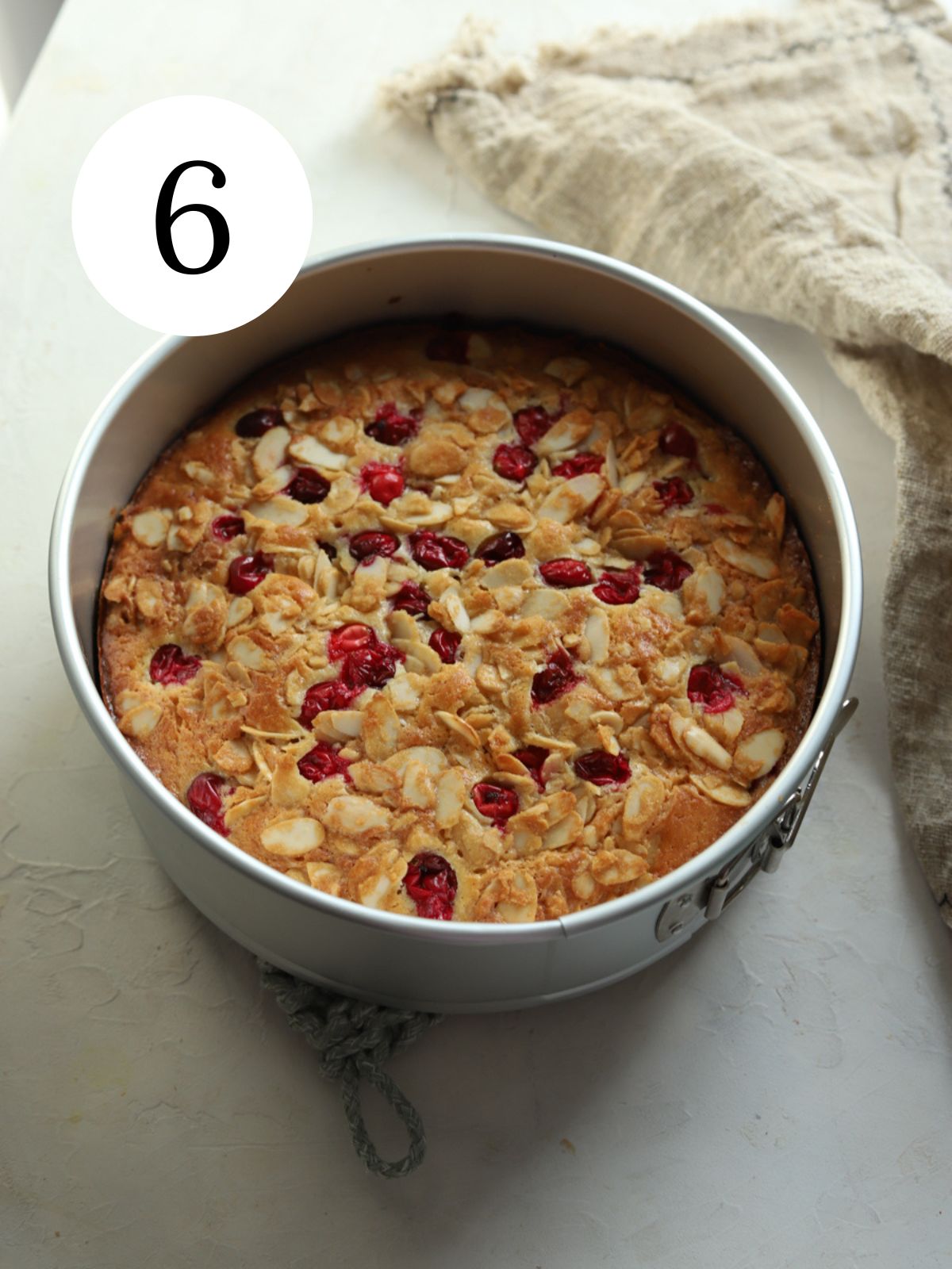 Cranberry almond cake in a round pan next to kitchen towel.