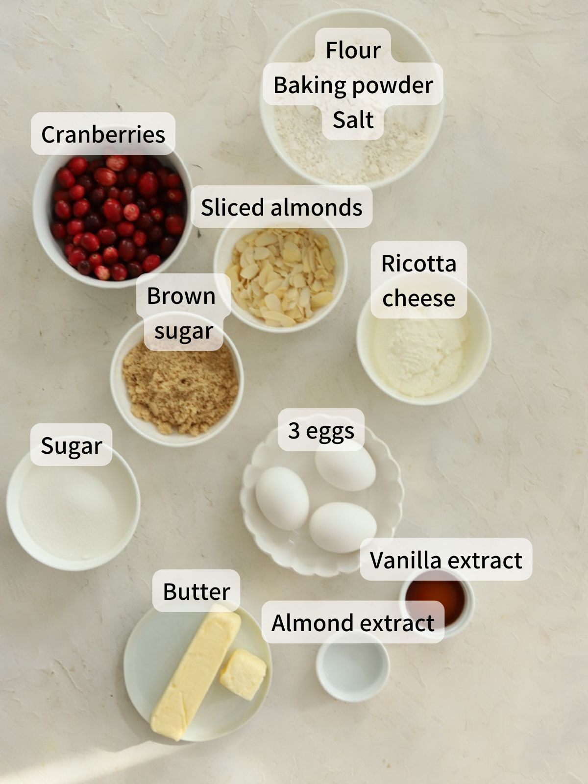 Labeled ingredients needed to make cranberry ricotta cake laid out on a table.