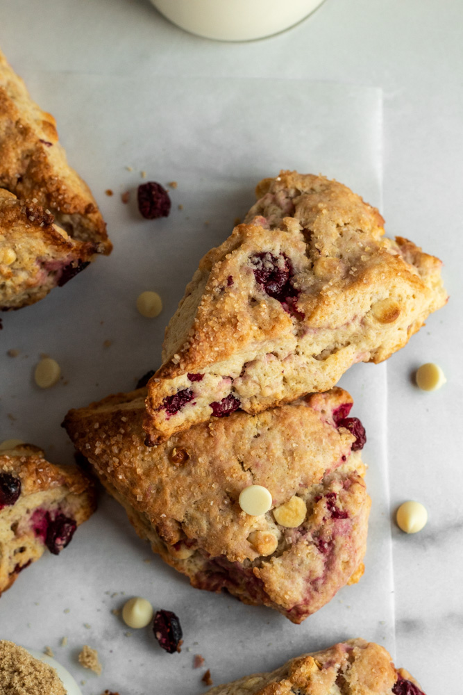 Homemade scones filled with cranberries and white chocolate chips on parchment paper. 