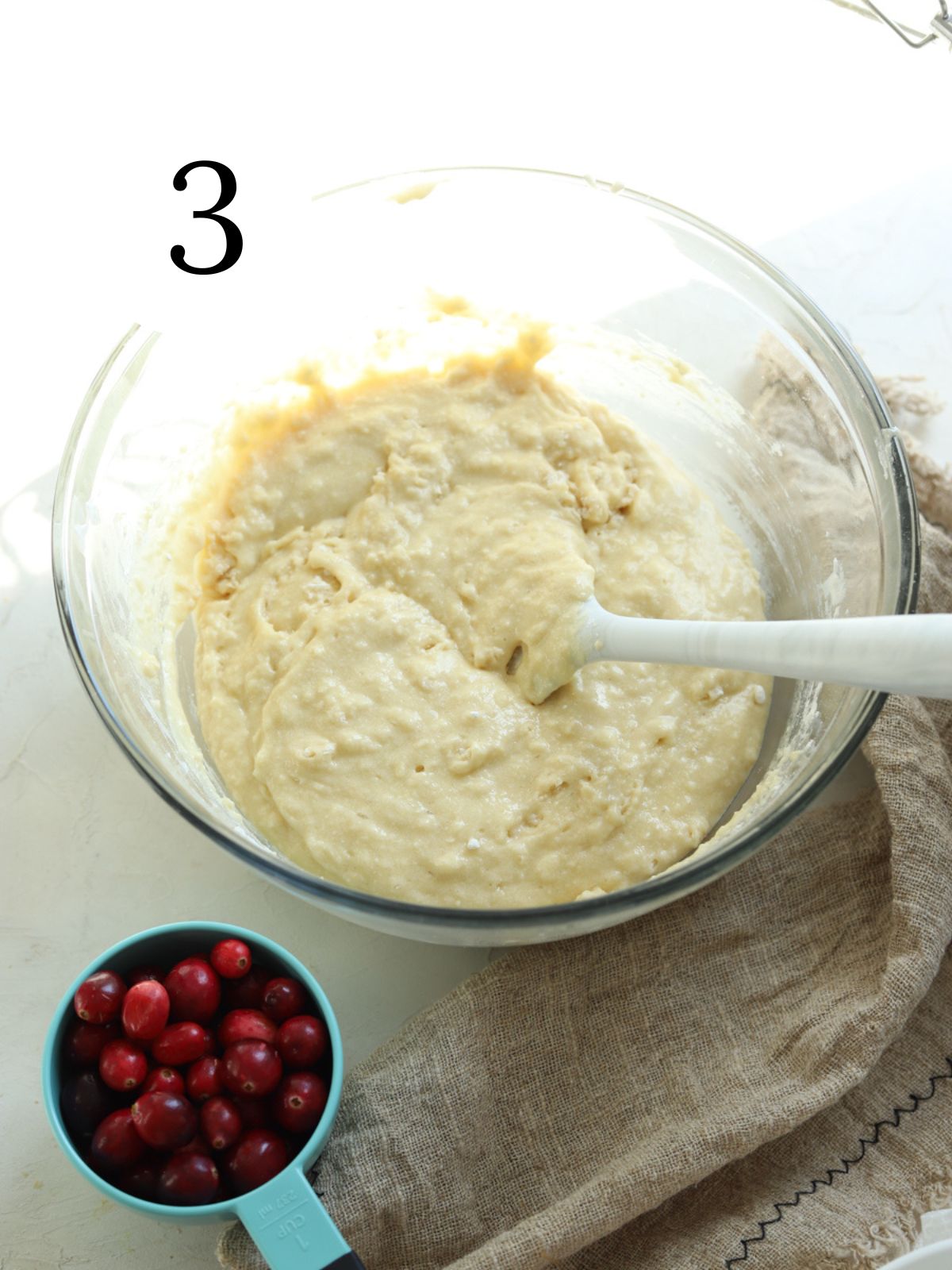 A glass mixing bowl with cake batter and a cup full of cranberries.
