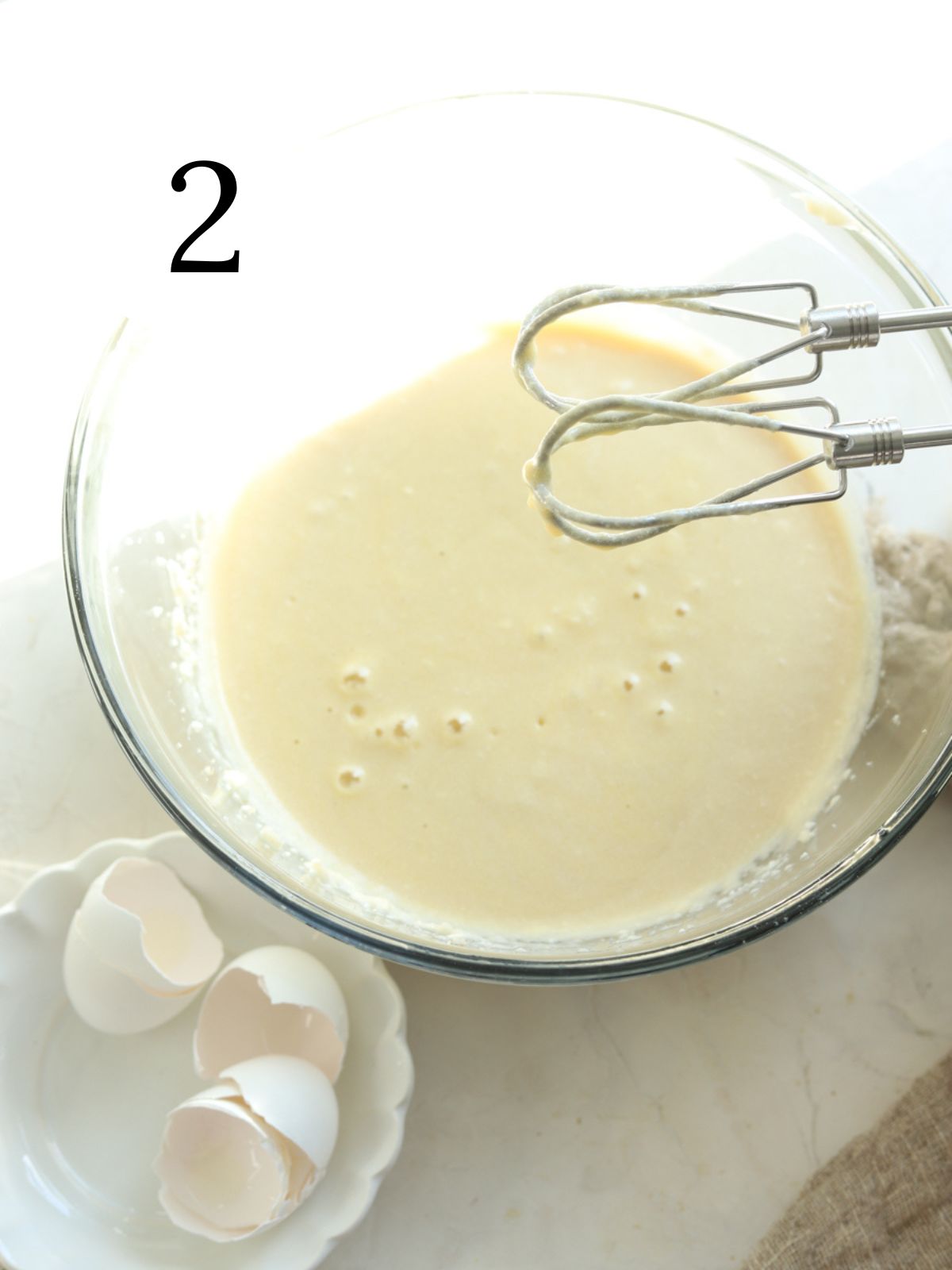 A mixing bowl with cake batter and an electric mixer next to some egg shells.