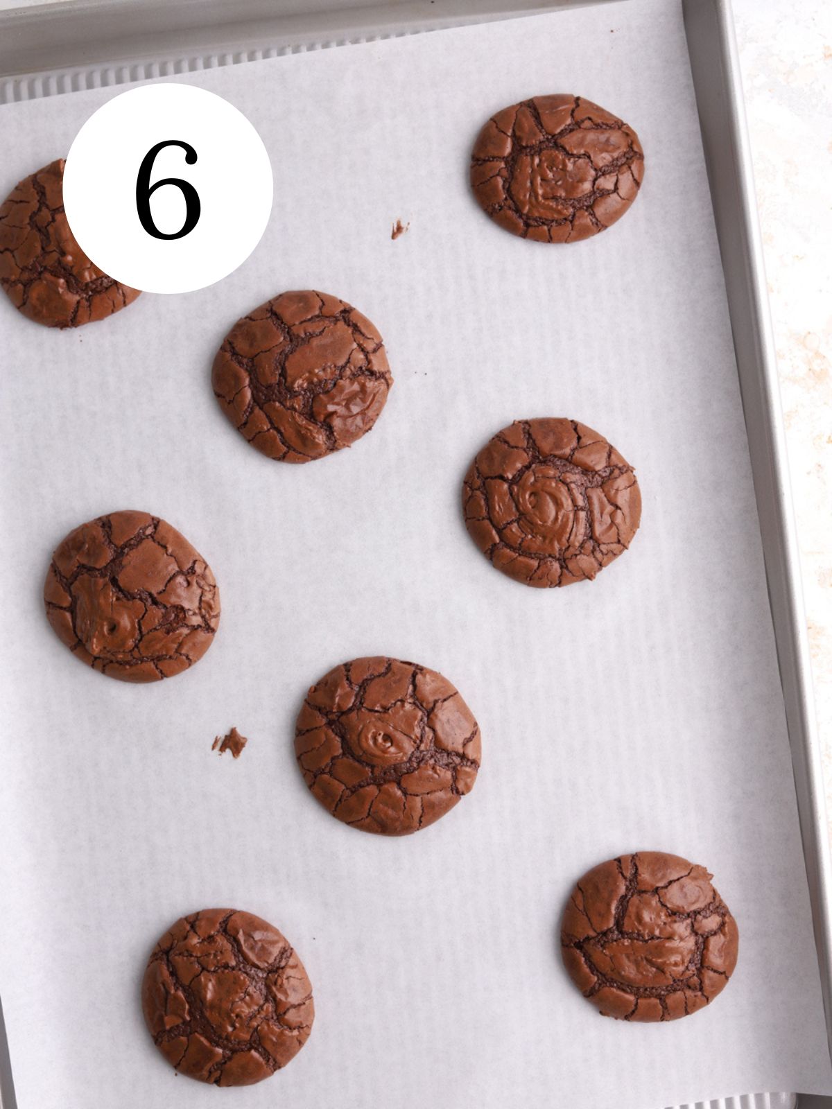 Freshly baked crackle topped chocolate cookies on a baking sheet. 