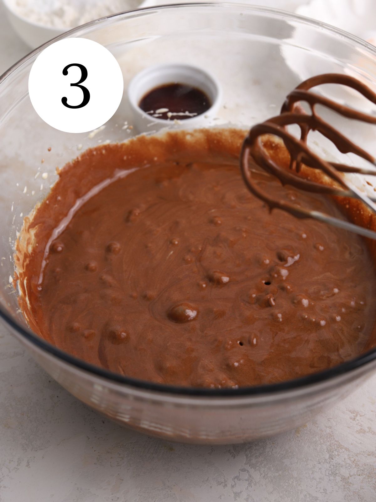 A glass bowl with brownie batter and an electric mixer. 