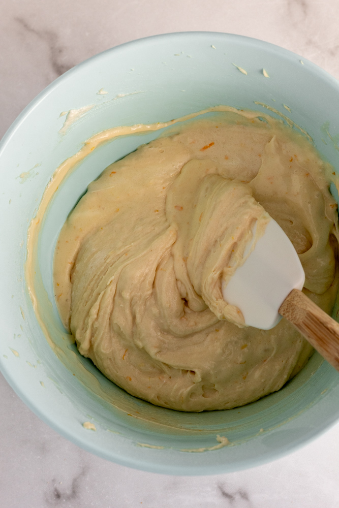 Cake batter with orange zest being mixed with a spatula in a bowl. 