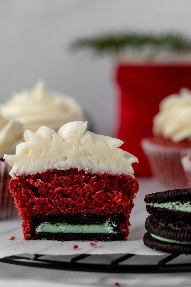 A red velvet cupcake sliced in half with a green Oreo inside and topped with frosting!