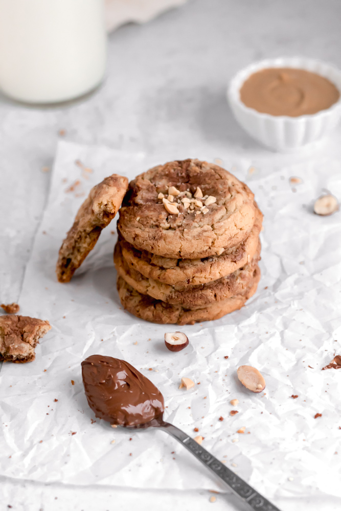 A stack of thick peanut butter cookies and a spoonful of Nutella.