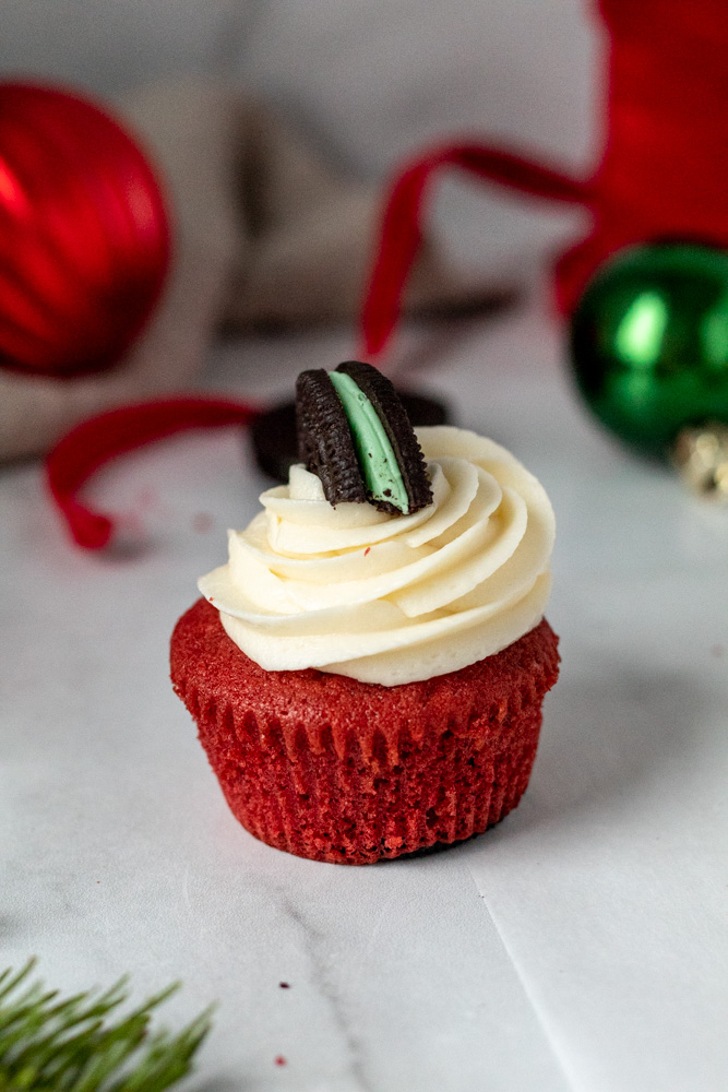 A close up of a red cupcake with swirls of frosting and an Oreo on top. 