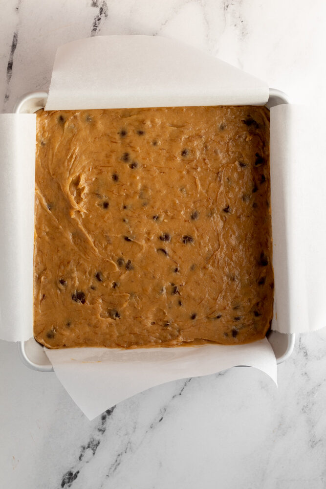 Delicious blondie batter with chocolate chips in it in a parchment paper lined pan. 