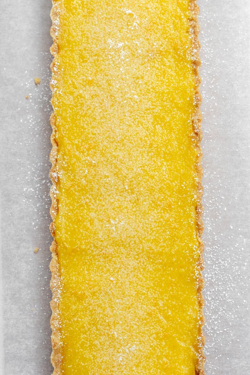A bright yellow rectangular lemon tart sprinkled with powdered sugar. 