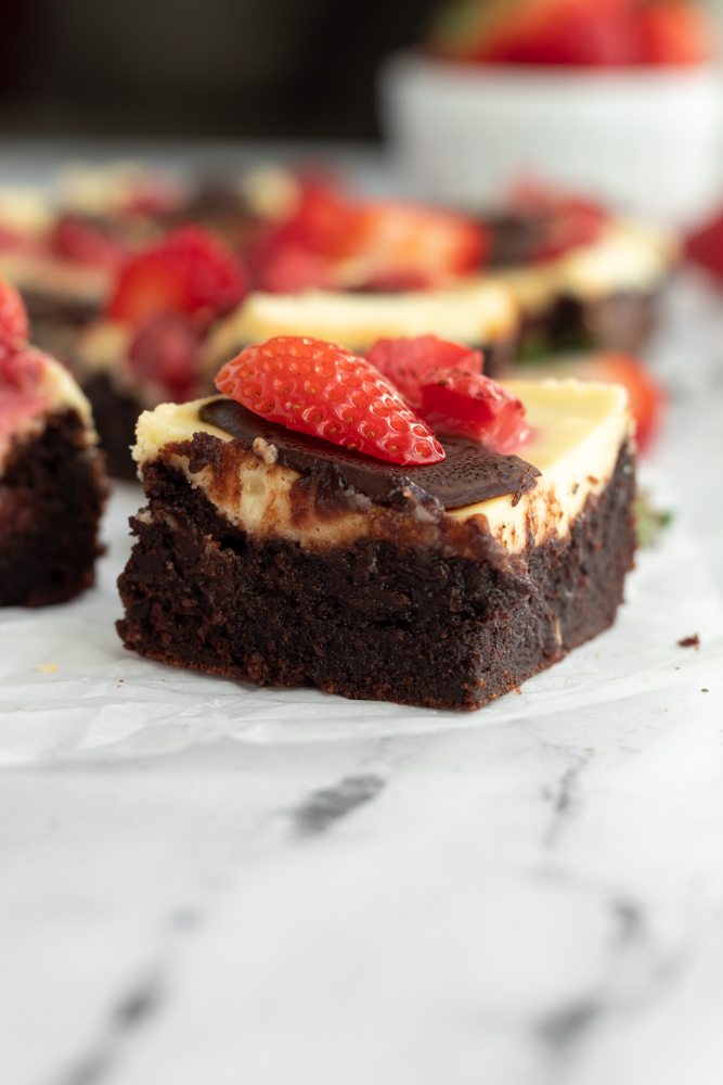 A chocolate brownie topped with cream cheese and strawberry slices.