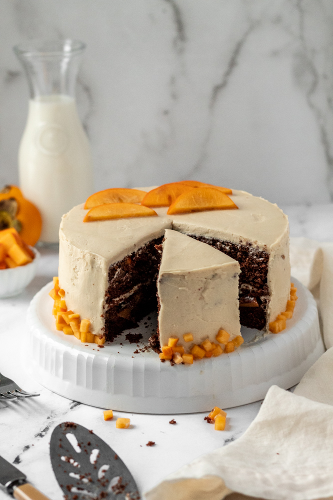 A chocolate layer cake with brown sugar icing topped with sliced persimmons. 