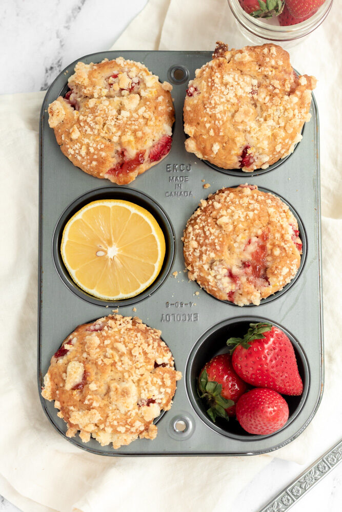 Strawberry muffins in a muffin tin with a lemon half and strawberries in the tin. 