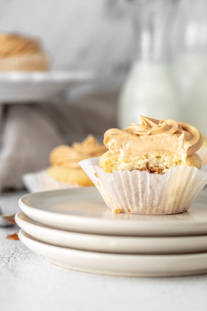 A cupcake topped with caramel colored frosting with a bite in it. 