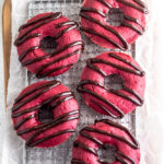 Red velvet donuts on a rack drizzled with chocolate.