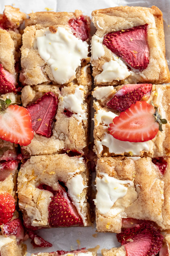 Blondies topped with lemon zest, white chocolate and berries cut into squares. 