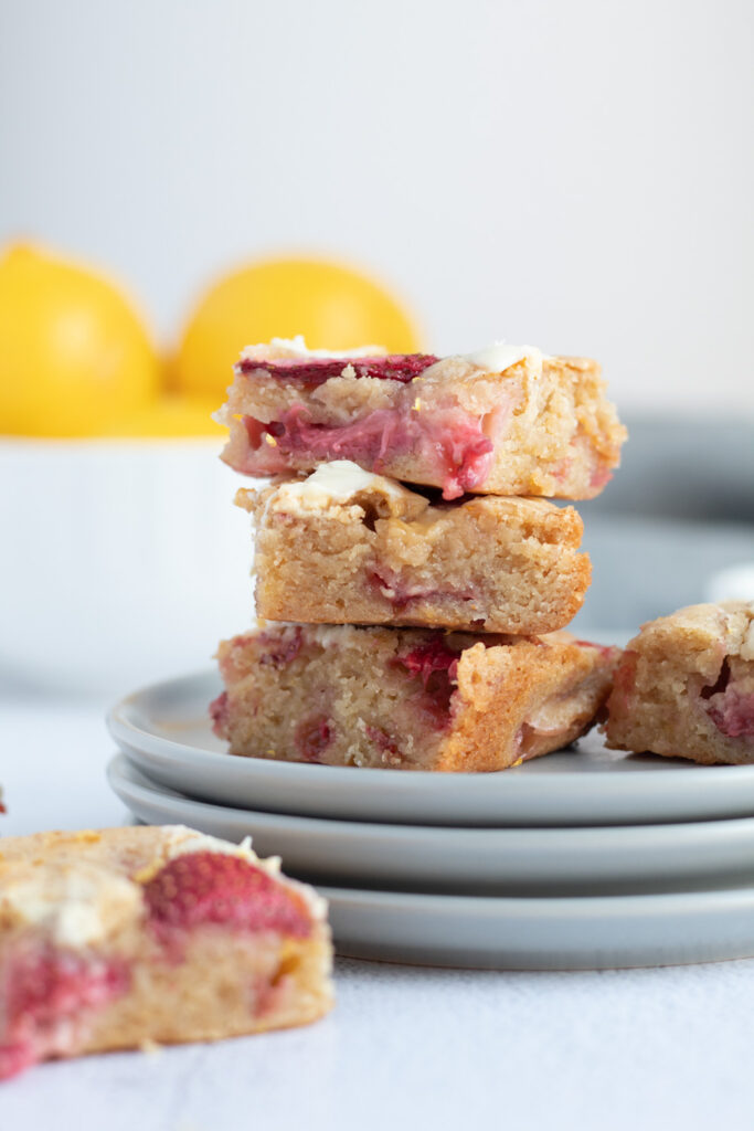 A stack of blondies with strawberries and a bowl of lemons.