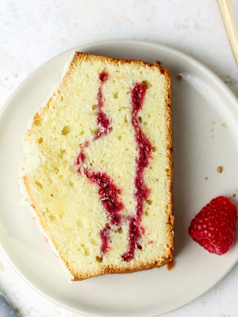 A piece of loaf cake with raspberry sauce in the middle on a small plate.