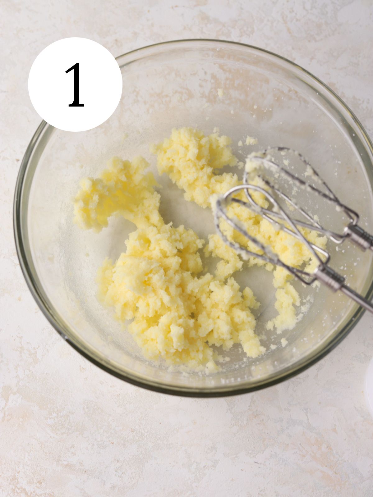 A glass mixing bowl with creamed butter and sugar and an electric mixer. 