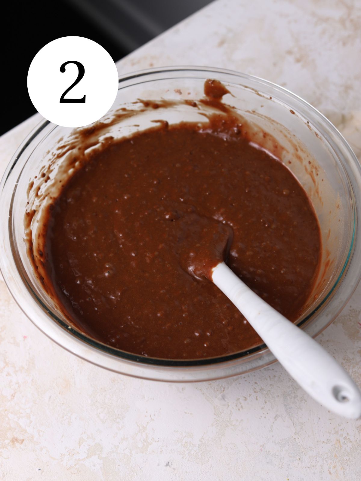 Chocolate cake batter in a glass bowl with a spatula. 