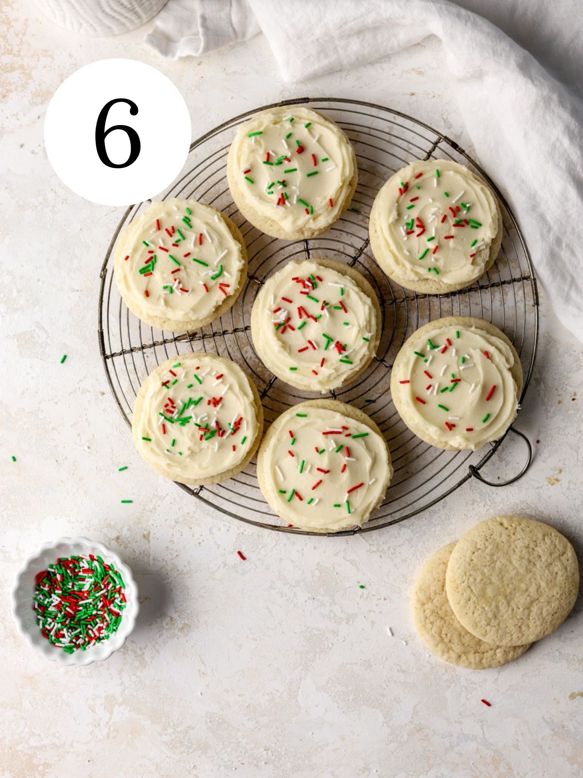 A batch of cookies with frosting and sprinkles on a rack and a bowl of sprinkles.