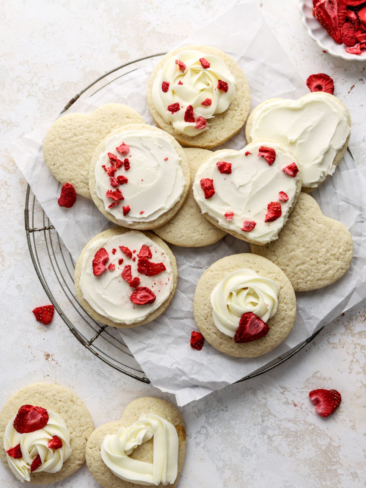 Frosted sugar cookies topped with freeze dried strawberries on a rack.