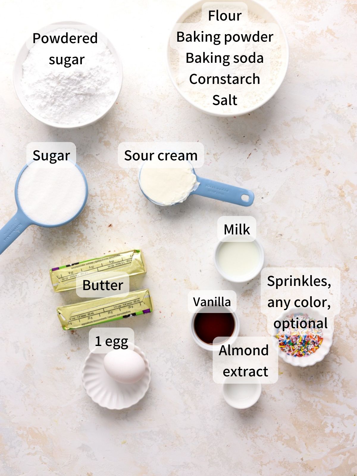 Labeled ingredients needed to make frosted sugar cookies laid out on a table. 