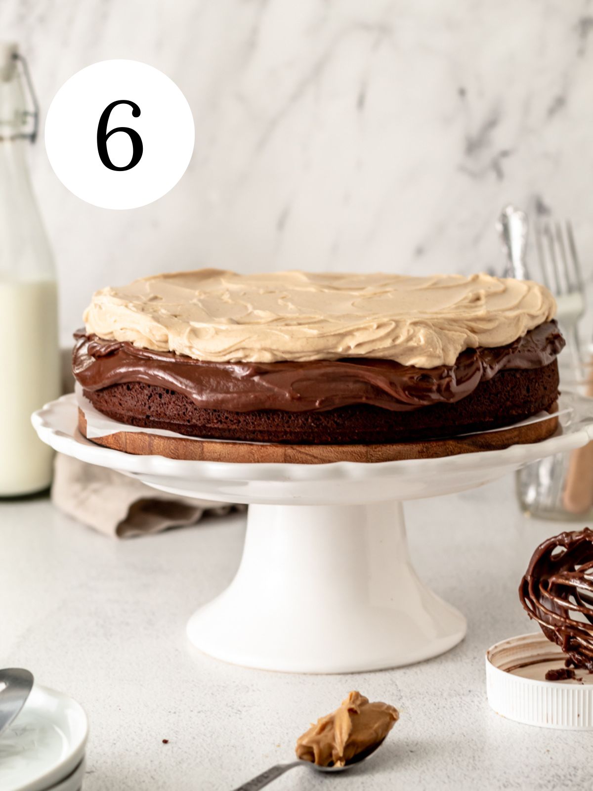 Chocolate cake topped with ganache and peanut butter frosting on a cake stand.